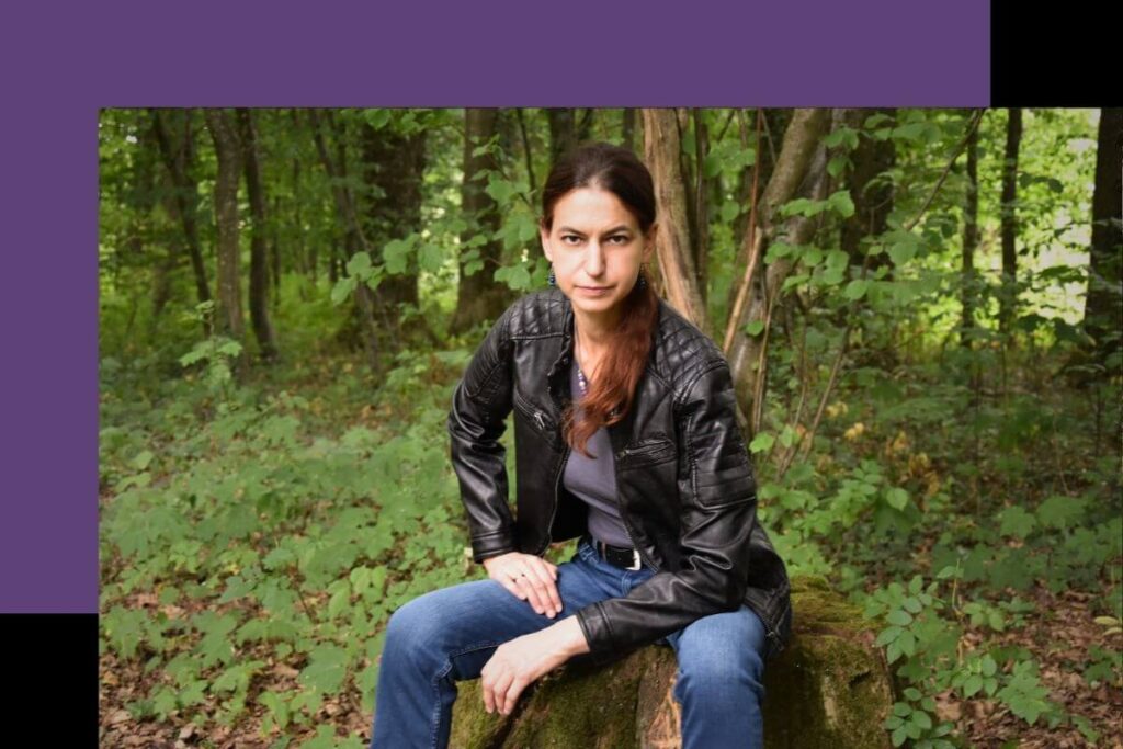 Fantasy-Autorin sitzt im Wald auf einem Baumstumpf.